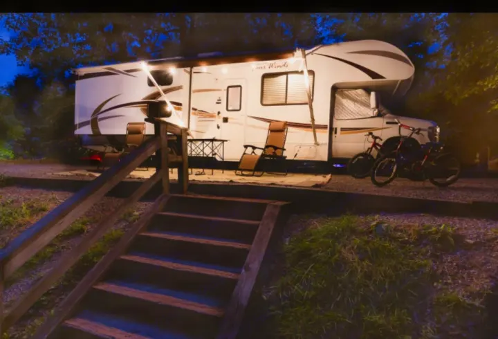 Evening campsite scene: A well-lit rv rental with chairs and bikes, accessible by wooden stairs.. Other Four Winds 2013