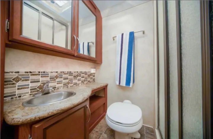 This RV rental bathroom features a sink, toilet, shower, and vanity with wood cabinets and a decorative tiled backsplash.. Other Four Winds 2013