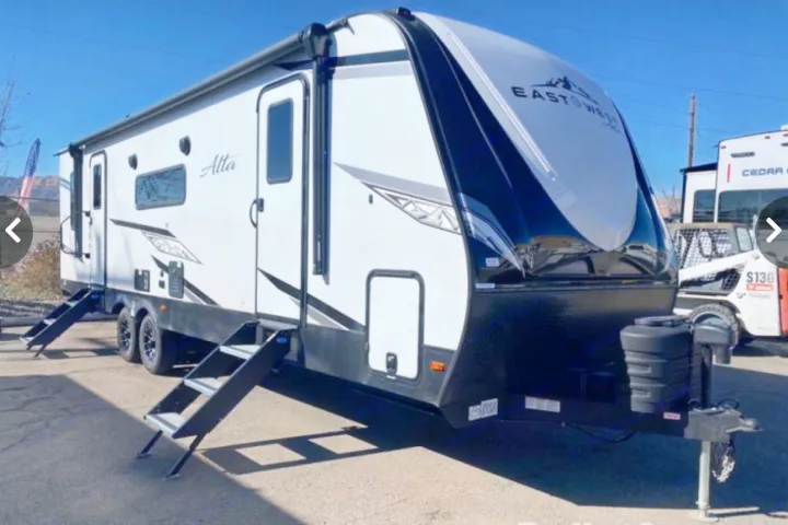 A white and black East to West Atta travel trailer, shown parked. This RV rental is ready with two entry doors and an awning.. East to West Alta 2022