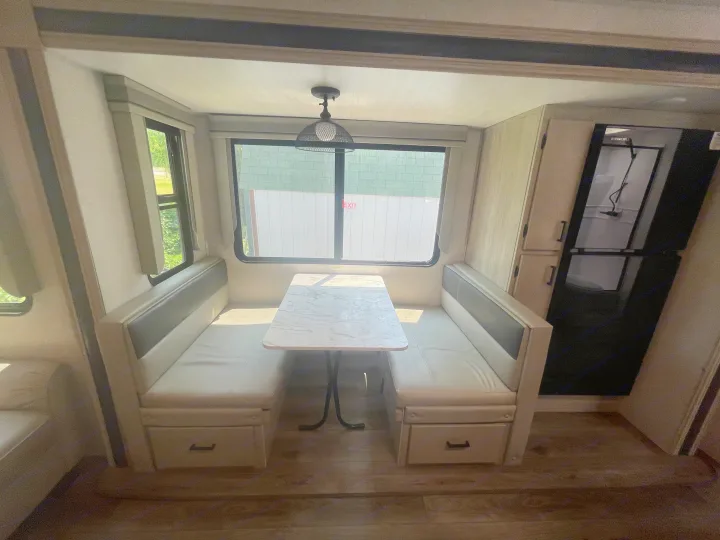 RV rental interior: A compact dinette with table & benches, near a fridge & windows for cozy travel dining.. East to West Alta 2022