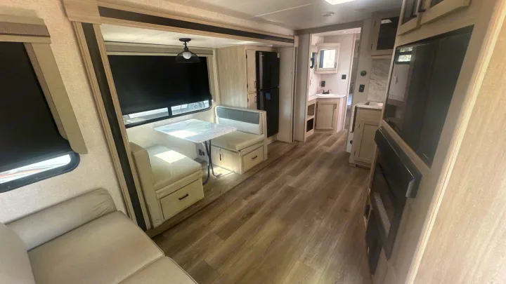 Spacious RV rental interior: light-colored living area, dining booth, kitchen, and bathroom. Ready for travel.. East to West Alta 2022