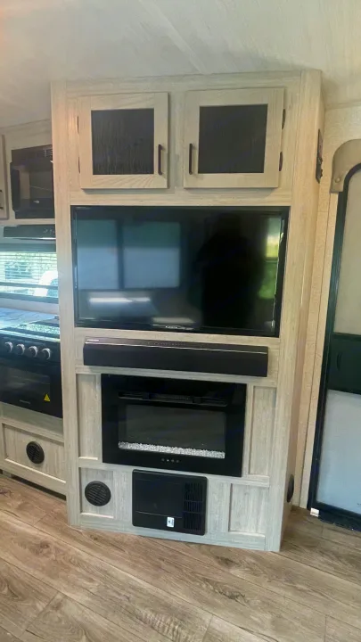Inside an RV rental: entertainment center featuring a TV, soundbar, and electric fireplace, next to kitchen appliances.. East to West Alta 2022