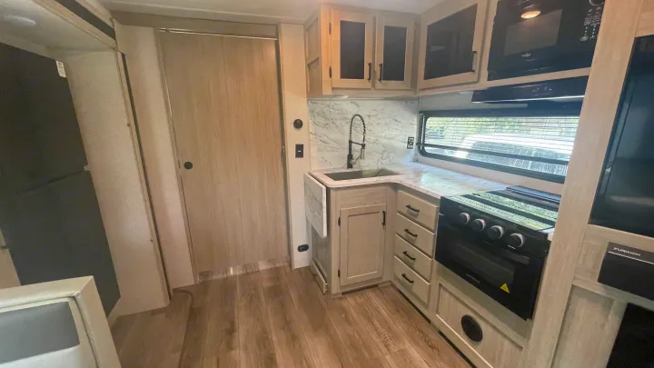 Explore this modern RV rental kitchen, featuring a full-size refrigerator, microwave, stove/oven, and sink with ample counter space.. East to West Alta 2022