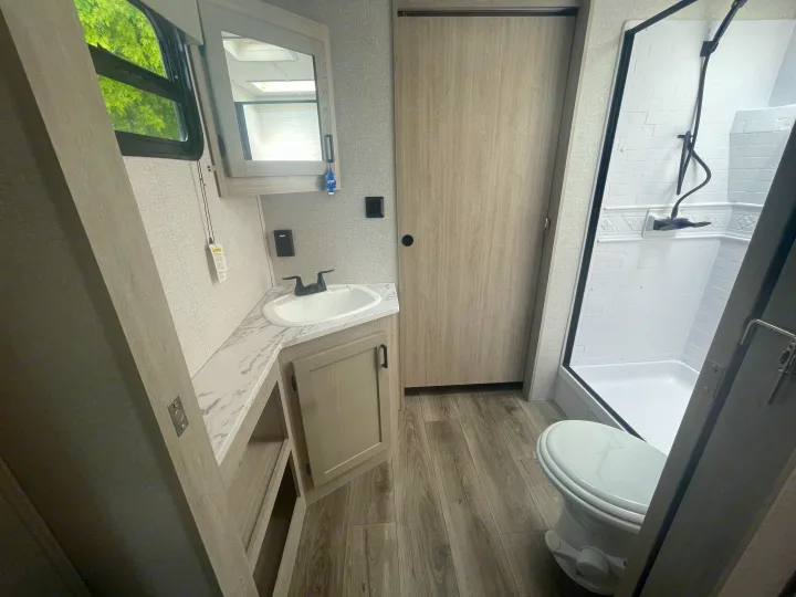 Clean and modern RV rental bathroom showcasing a sink vanity, mirror cabinet, toilet, shower, and light wood finishes.. East to West Alta 2022