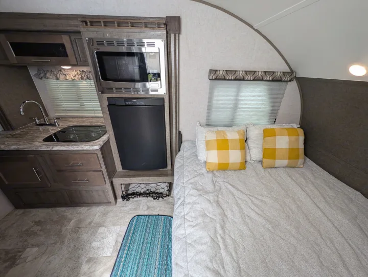 Inside an RV rental, featuring a functional kitchenette with a microwave/fridge, plus a cozy bed with yellow plaid pillows.. Forest River R Pod 2018