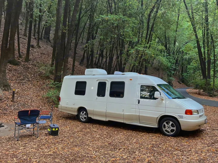 RV rental parked in a tranquil forest campsite with chairs and cooler ready for a relaxing outdoor getaway.. Winnebago Rialta 2003