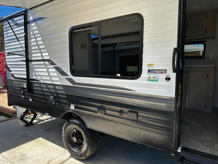 View of an RV rental travel trailer's side: extended awning, large window, and open door with interior visible. Includes tire & leveling jack.. Forest River EVO 2024