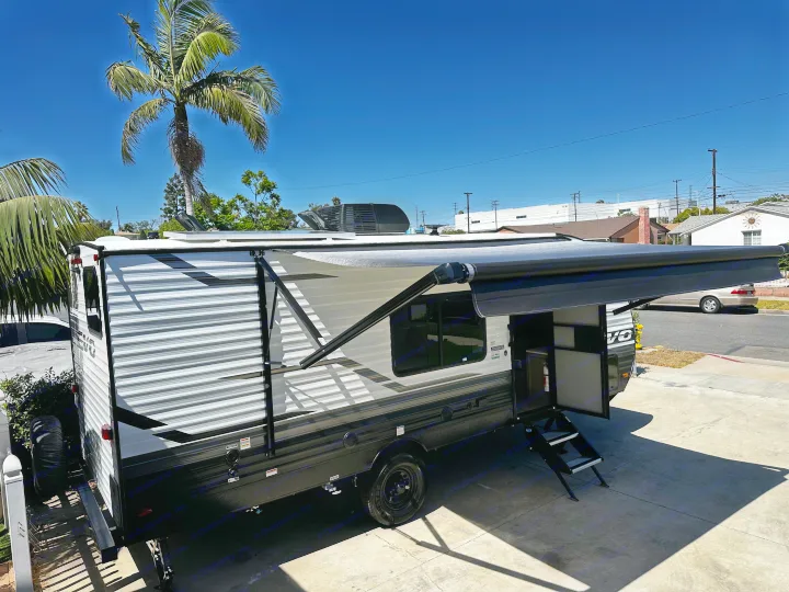 This RV rental travel trailer is parked with its awning out & steps down, perfect for a sunny day trip.. Forest River EVO 2024