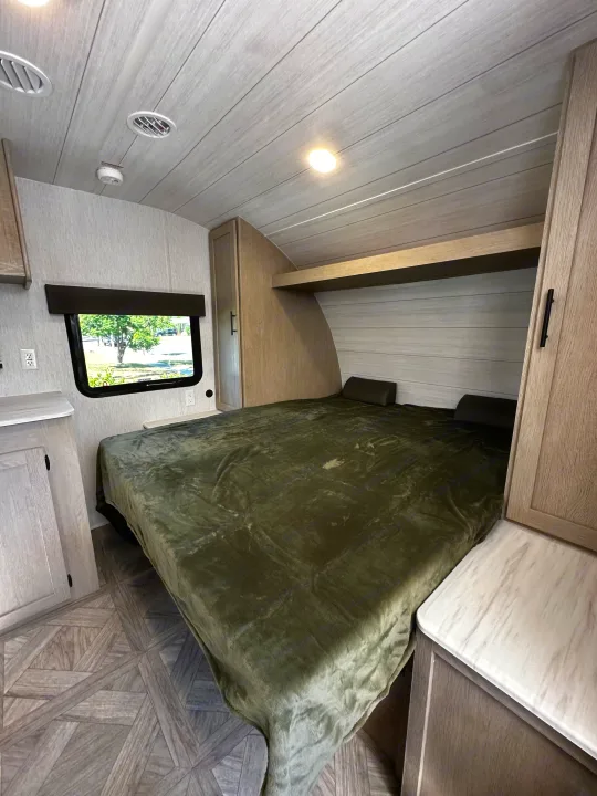 Inside a modern RV rental bedroom featuring a comfy bed, window view of trees, and light wood cabinetry.. Forest River EVO 2024