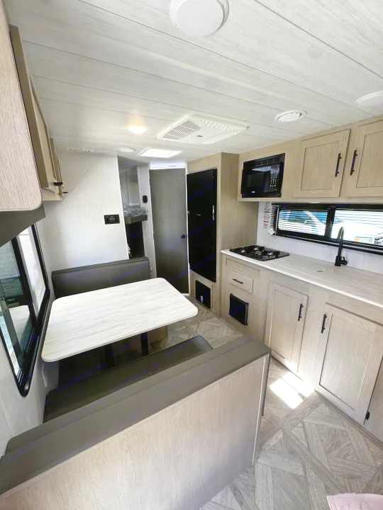Bright RV rental interior: Features a modern kitchen with stove/microwave, a dinette, and bunk beds visible in the rear.. Forest River EVO 2024