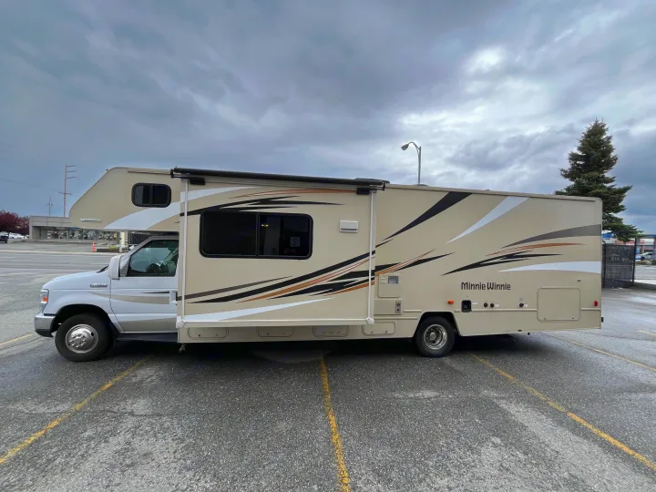A beige Minnie Winnie RV rental parked on a paved lot under a cloudy sky, ready for your next adventure.. Winnebago Minnie Winnie 2017