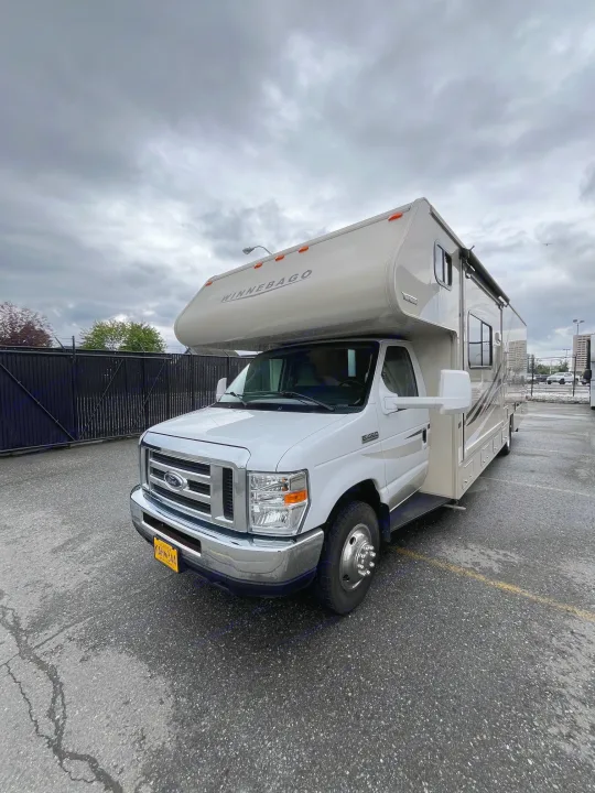 A white Winnebago Class C RV rental is parked on asphalt under a cloudy sky, awaiting its next adventure.. Winnebago Minnie Winnie 2017