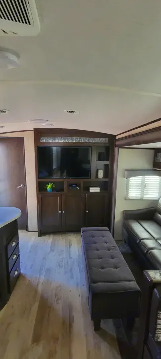 RV rental living area with a dark wood entertainment center, TV, plush bench, and leather sofa.. Heartland Sundance 2019