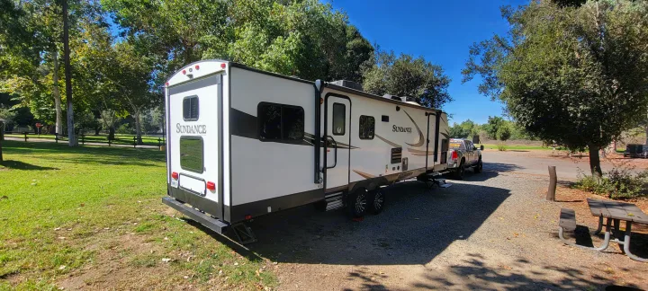 A white Sundance travel trailer (RV rental) and pickup truck at a sunny park campsite, perfect for camping.. Heartland Sundance 2019
