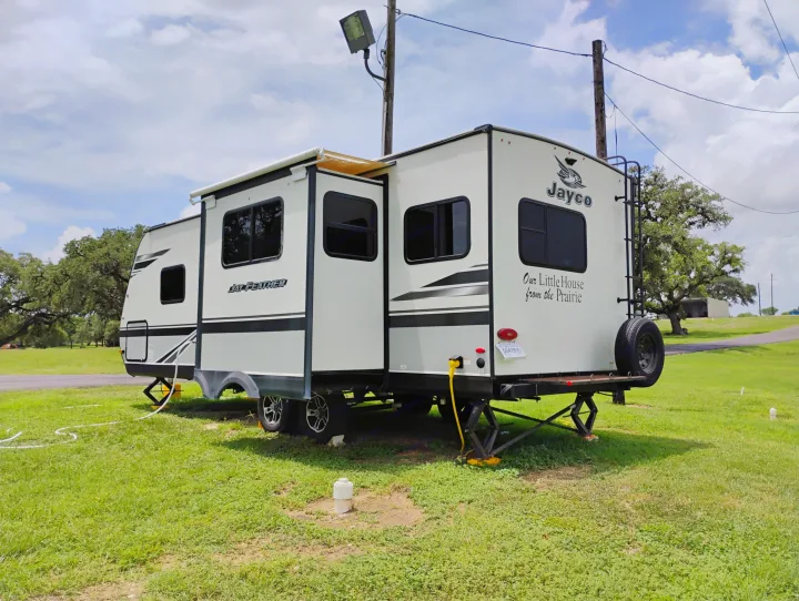This Jayco RV rental travel trailer is set up on green grass for a relaxing camping trip, featuring an extended awning and utility connections.. Jayco Jay Feather 2021