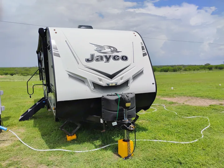 This Jayco RV rental is fully set up in a scenic green field, ready for your adventure. Note the extended steps and utility hookups.. Jayco Jay Feather 2021