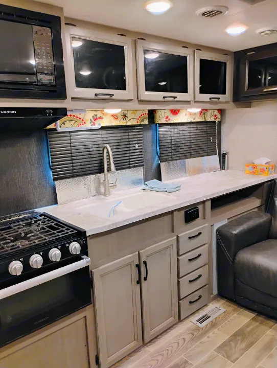 RV rental kitchen interior: Modern stove, microwave, sink, spacious countertop, cabinetry, and a cozy seating area.. Jayco Jay Feather 2021