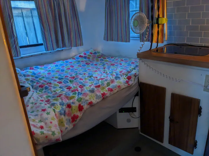 Cozy RV rental interior with a comfy floral bed, windows with striped curtains, and a compact kitchen. Ideal for travel!. Boler Boler 1300 1974