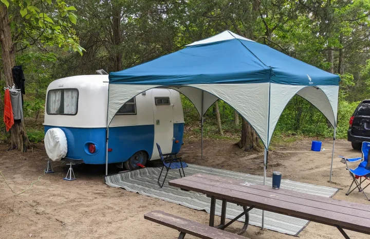 Vintage RV rental setup at a shaded campsite with a canopy, picnic table, and chairs for outdoor enjoyment.. Boler Boler 1300 1974
