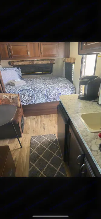 Cozy RV rental interior with a patterned bed, compact kitchen, and dinette. Ideal for comfortable travel.. Jayco Jay Flight 2018