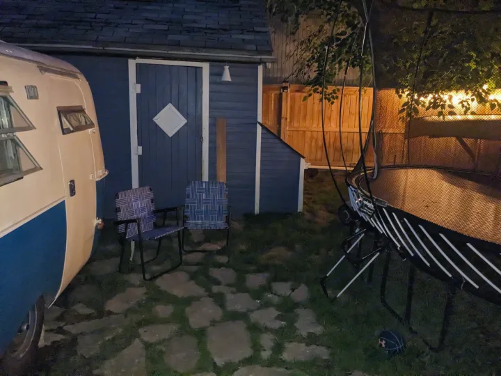 Evening view of an RV rental, blue shed, chairs, & trampoline in a backyard with stone path.. Boler Boler 1300 1974
