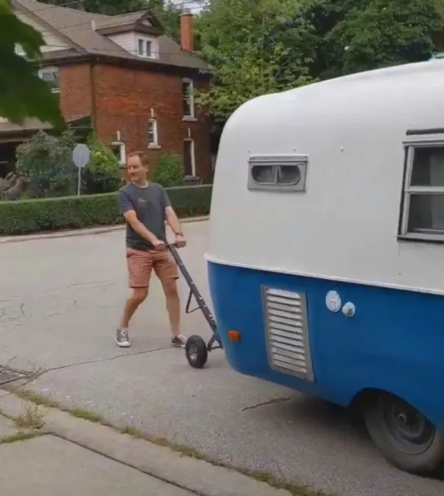 A man manually moves a retro **RV rental** with a dolly on a residential street.. Boler Boler 1300 1974