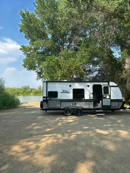 RV rental: Jay Flight travel trailer parked by a tranquil river, shaded by large trees, perfect for an outdoor escape.. Jayco Jay Flight SLX 2024