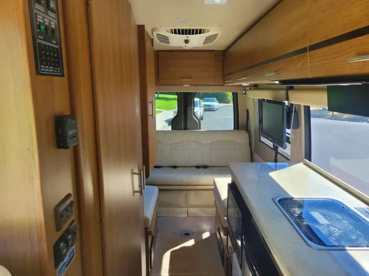 RV rental interior: Looking towards the back, shows cream seating, a compact kitchenette, and a control panel on the left.. Winnebago Era 2016
