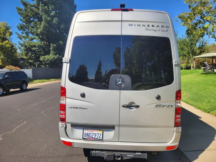 Silver Winnebago Sprinter rv rental van parked on a sunny street, showing its rear with California license plate.. Winnebago Era 2016