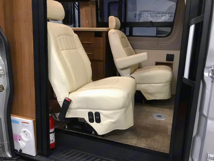 Comfortable cream captain's chairs inside an RV rental. Explore mobile living with this well-appointed camper van interior.. Winnebago Era 2016