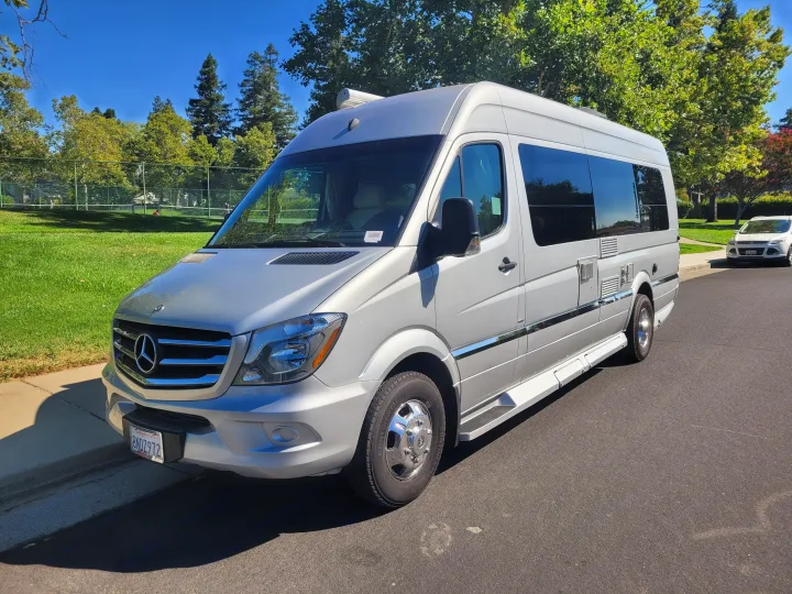 Explore in style with this silver Mercedes-Benz Sprinter RV rental. Parked curbside on a sunny day near a green park.. Winnebago Era 2016