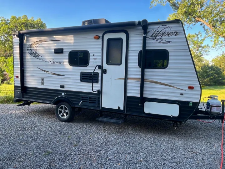 A white and black Coachmen Clipper travel trailer, a great RV rental option, is parked on gravel. Note the awning and propane tank.. Clipper Clipper Trailer 2016