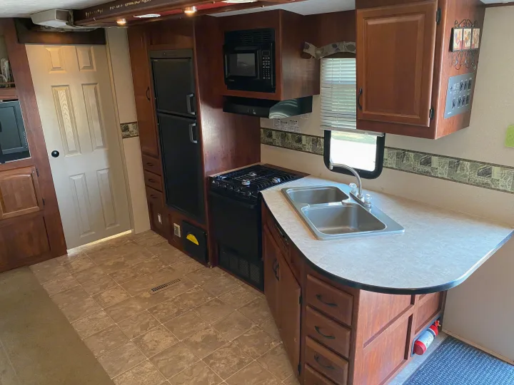 Explore this RV rental kitchen, featuring a double sink, gas stove, microwave, refrigerator, and ample wood cabinetry. Light tile flooring visible.. MVP Coast 2009