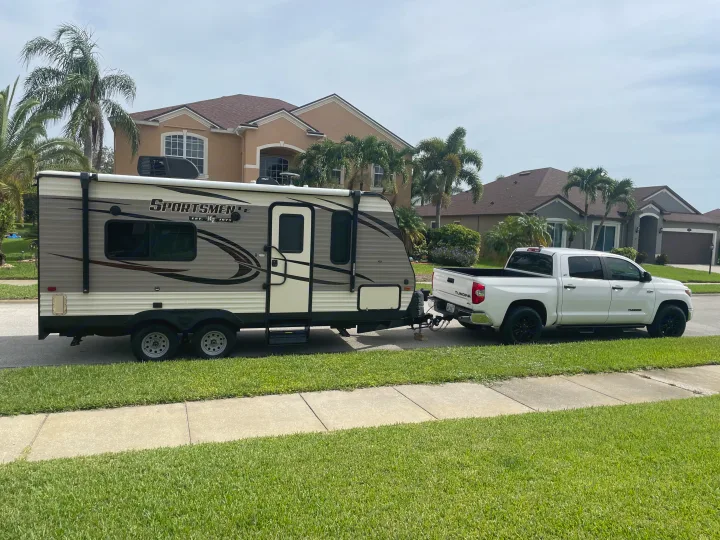 White pickup truck towing a Sportsmen travel trailer, perfect for an RV rental adventure, parked on a residential street.. KZ Sportsmen 2019
