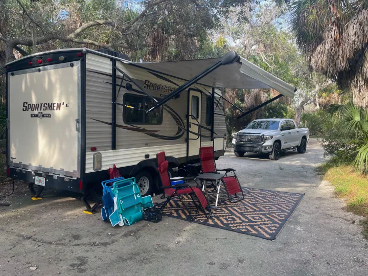An RV rental, truck, and shaded campsite setup with chairs and a rug for a relaxing outdoor getaway.. KZ Sportsmen 2019