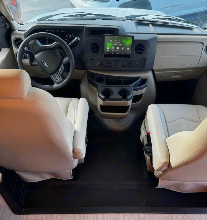 View of an RV rental's spacious front cabin with light-colored seats, steering wheel, infotainment screen, and cup holders.. Jayco Greyhawk 2021