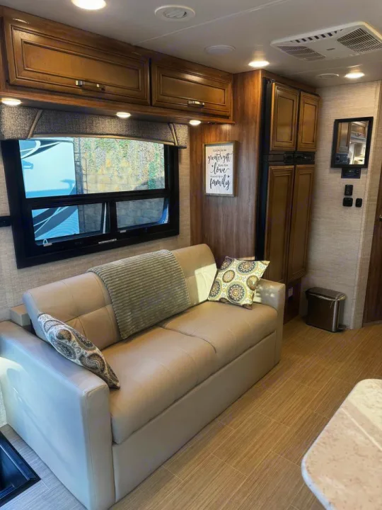Spacious RV rental interior with a comfy sofa, wooden cabinets, and a large window.. Jayco Greyhawk 2021