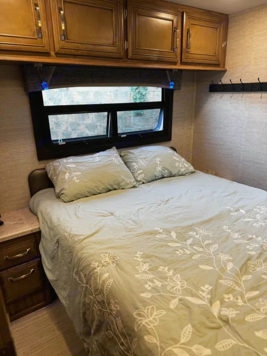 Cozy RV rental bedroom with floral bedding, overhead cabinets, and window view. Perfect for your next adventure.. Jayco Greyhawk 2021