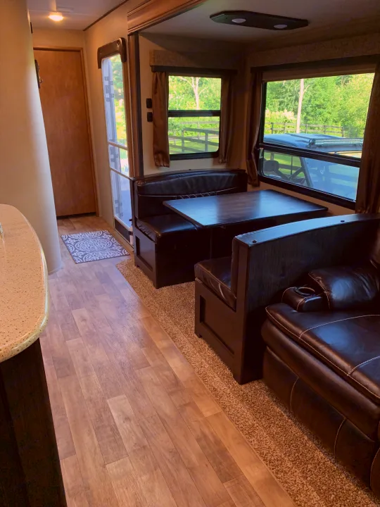 Inside a spacious RV rental: a comfortable dinette, leather sofa, and kitchen counter, offering bright views of nature.. Reflection BHT33 2018