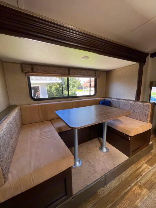 Cozy RV rental dinette with U-shaped beige seating, wood-look table, and large windows. Perfect for dining & relaxing.. Forest River Cherokee Grey Wolf 2017