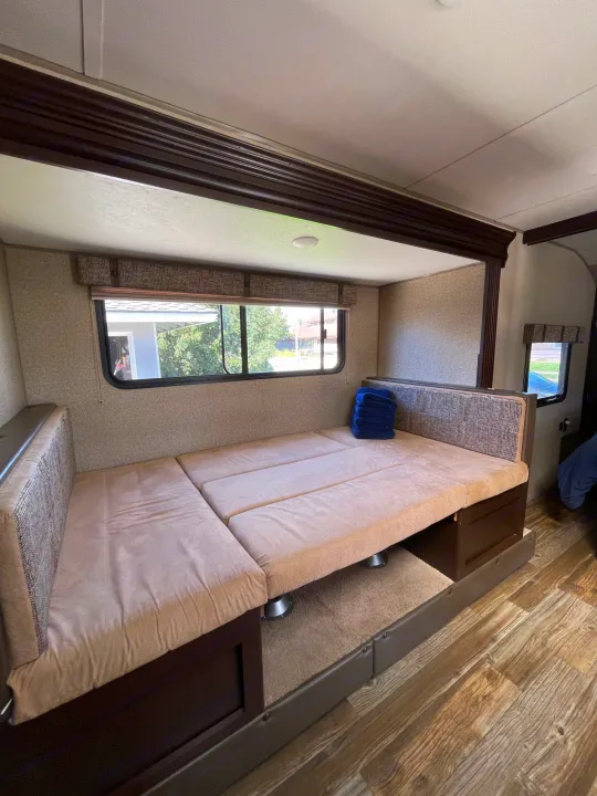 Inside an RV rental, a comfy dinette converts to a bed with beige cushions and wide windows.. Forest River Cherokee Grey Wolf 2017