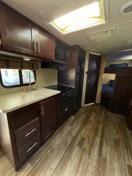 Spacious RV rental interior featuring a full kitchen, refrigerator, bunk beds, and wood-look flooring.. Forest River Cherokee Grey Wolf 2017