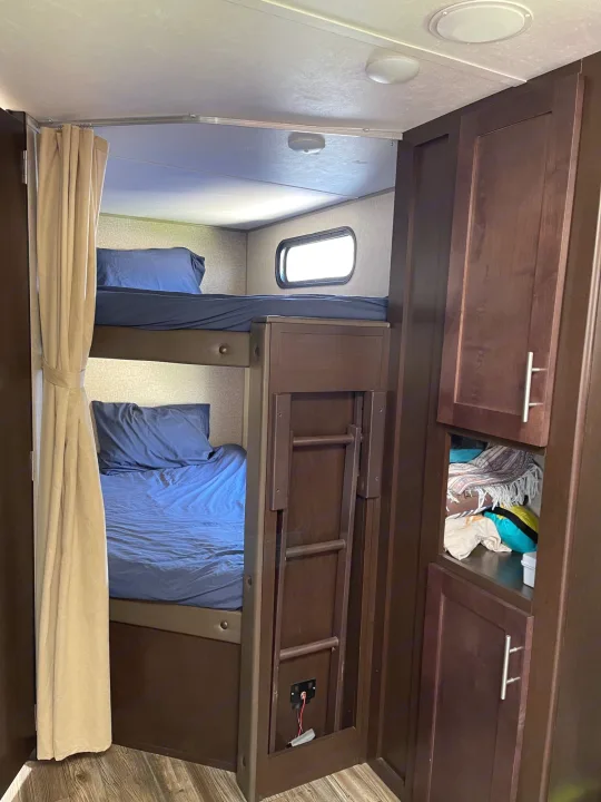 Cozy RV rental bunk beds with blue linens, featuring a folding ladder and storage cabinets, perfect for family adventures.. Forest River Cherokee Grey Wolf 2017