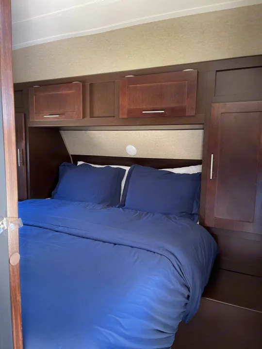 Cozy RV rental bedroom with dark wood cabinets, a light headboard, and a neatly made bed with navy blue bedding.. Forest River Cherokee Grey Wolf 2017