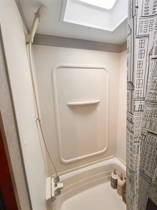 Compact RV rental shower interior with a handheld showerhead, skylight, and city-themed shower curtain.. Keystone RV Hideout 2017