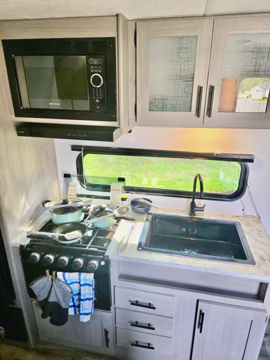 Inside an RV rental: a bright kitchen with a microwave, stove, sink, and scenic window view. Modern comforts on the road.. Coleman Coleman lantern lt 2024