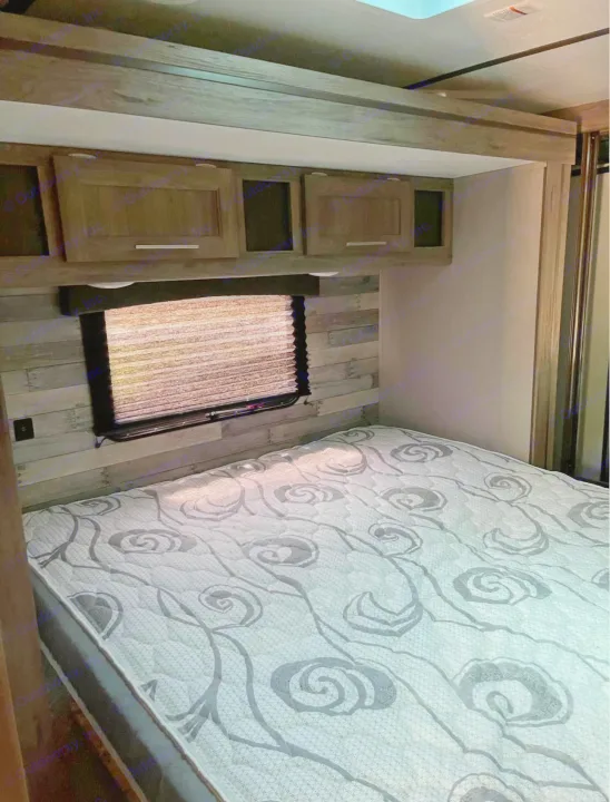 Cozy RV rental bedroom with a patterned bed, window with blinds, and overhead storage. Perfect for travel.. Crossroads RV Zinger 2020
