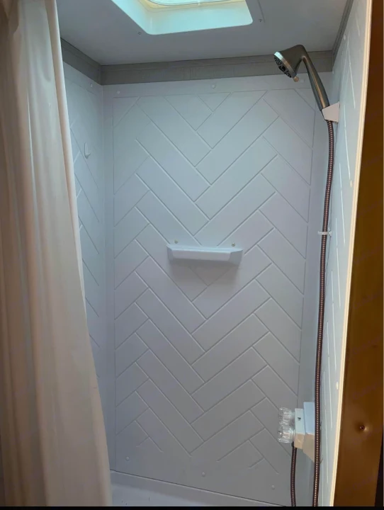 Inside an RV rental shower: white herringbone-patterned walls, a showerhead, and control knobs. A skylight brightens the space.. Crossroads RV Zinger 2020