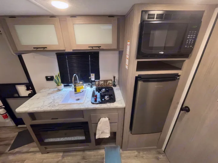 RV rental: Compact kitchenette featuring an overhead microwave, lower fridge, counter with sink, stove, and light wood cabinets.. Coleman lantern lt 17b 2024