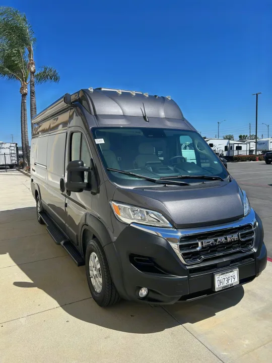 Dark grey Ram ProMaster camper van, ready for rv rental, parked on concrete under a blue sky near palm trees.. Thor Tellaro 2024